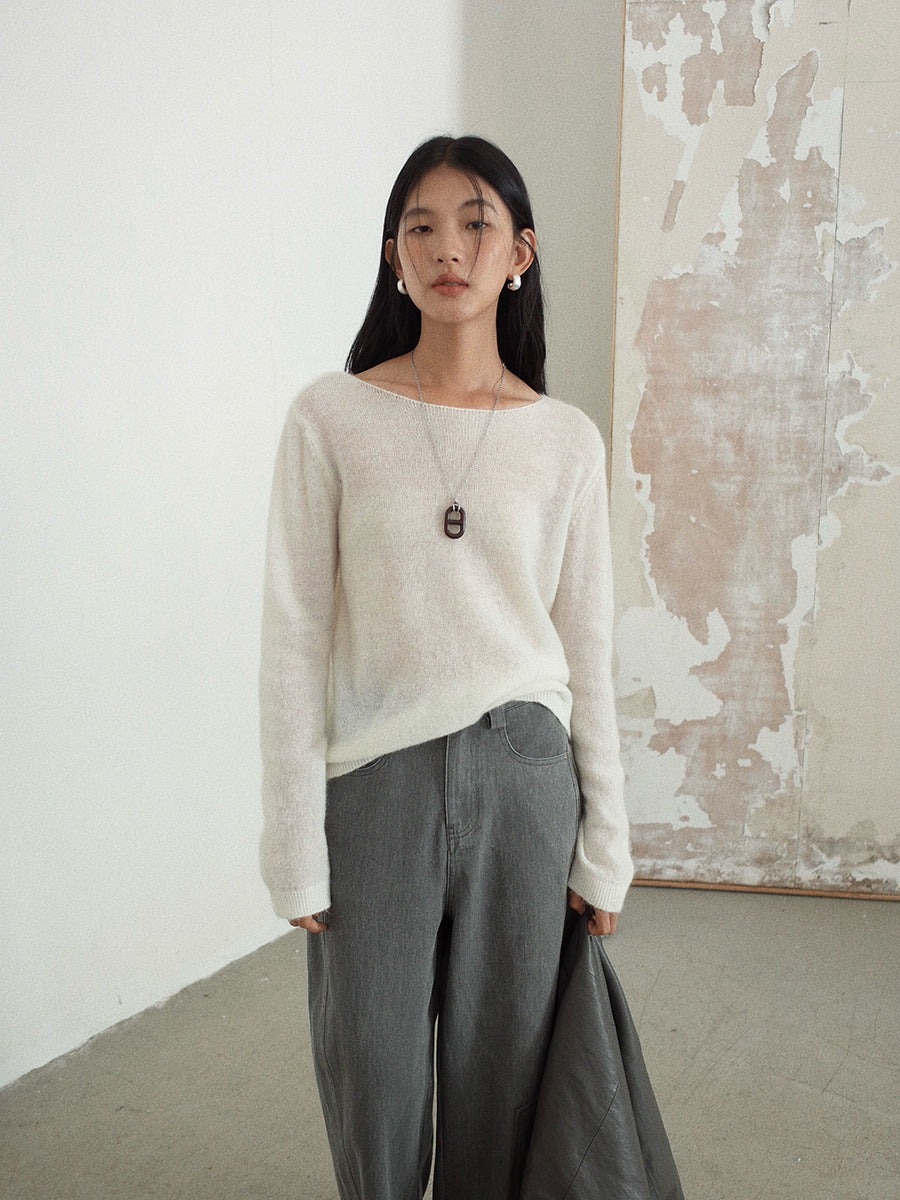 Woman wearing a white wool pullover sweater and gray pants standing against a plain wall.