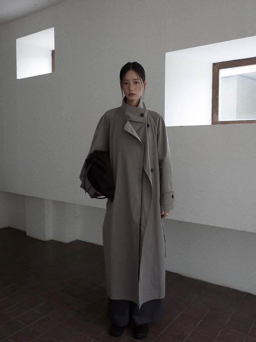Person wearing a long Stand-up Collar Long Trench Coat with Belt standing in a minimalistic room with white walls and a dark floor.