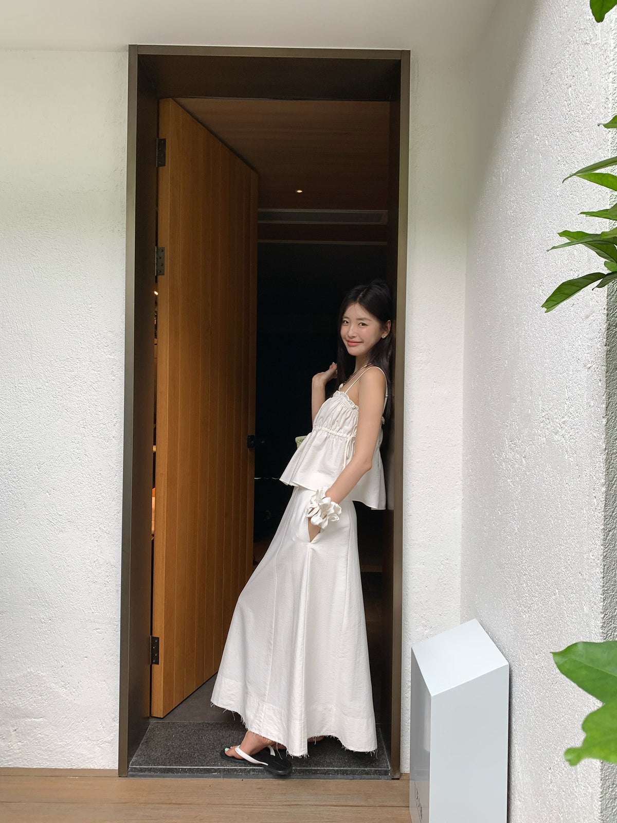 Woman in a white Two-Piece Raw Edge A-line Maxi Versatile Skirt Set standing in a doorway with a plant to the side.