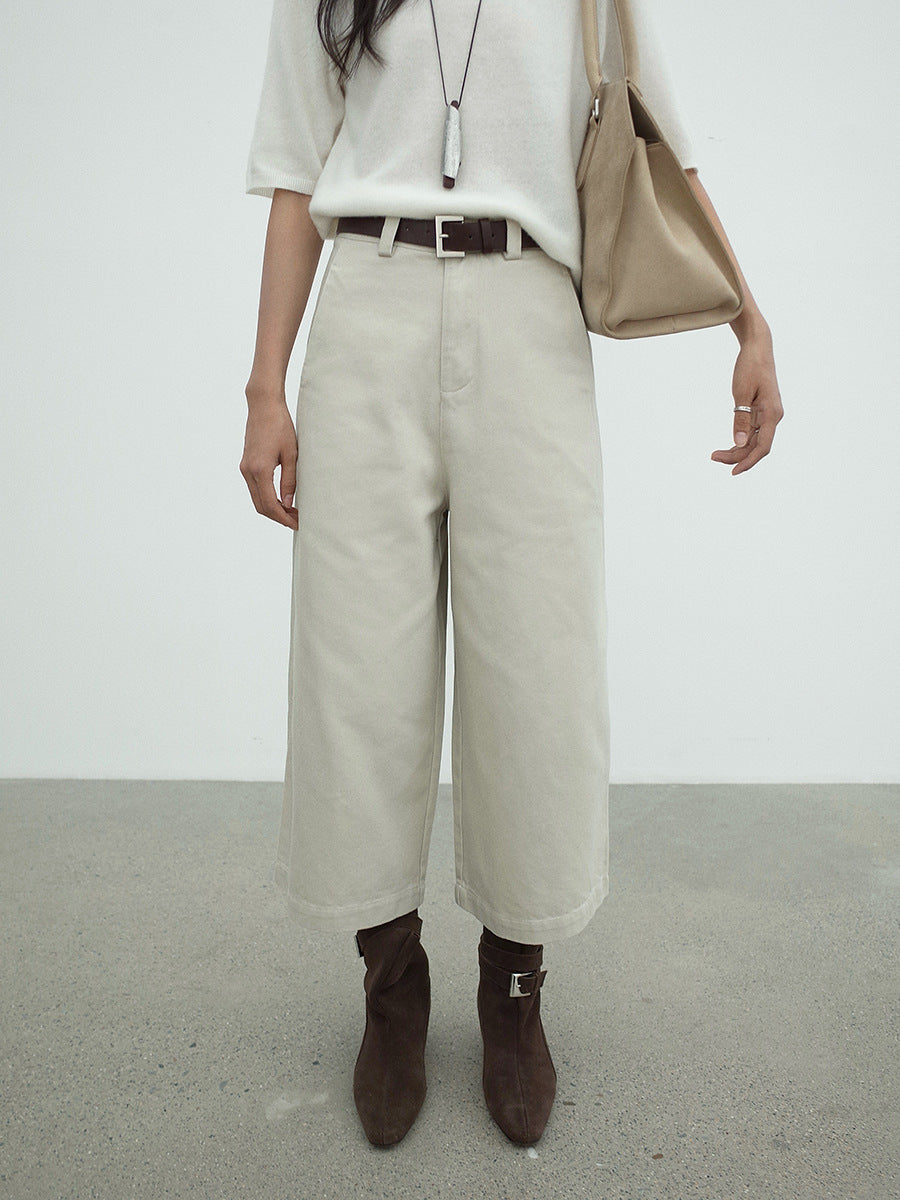 Person wearing beige Cropped Wide-Leg Straight Jeans, white shirt, and brown boots in a minimalistic setting.