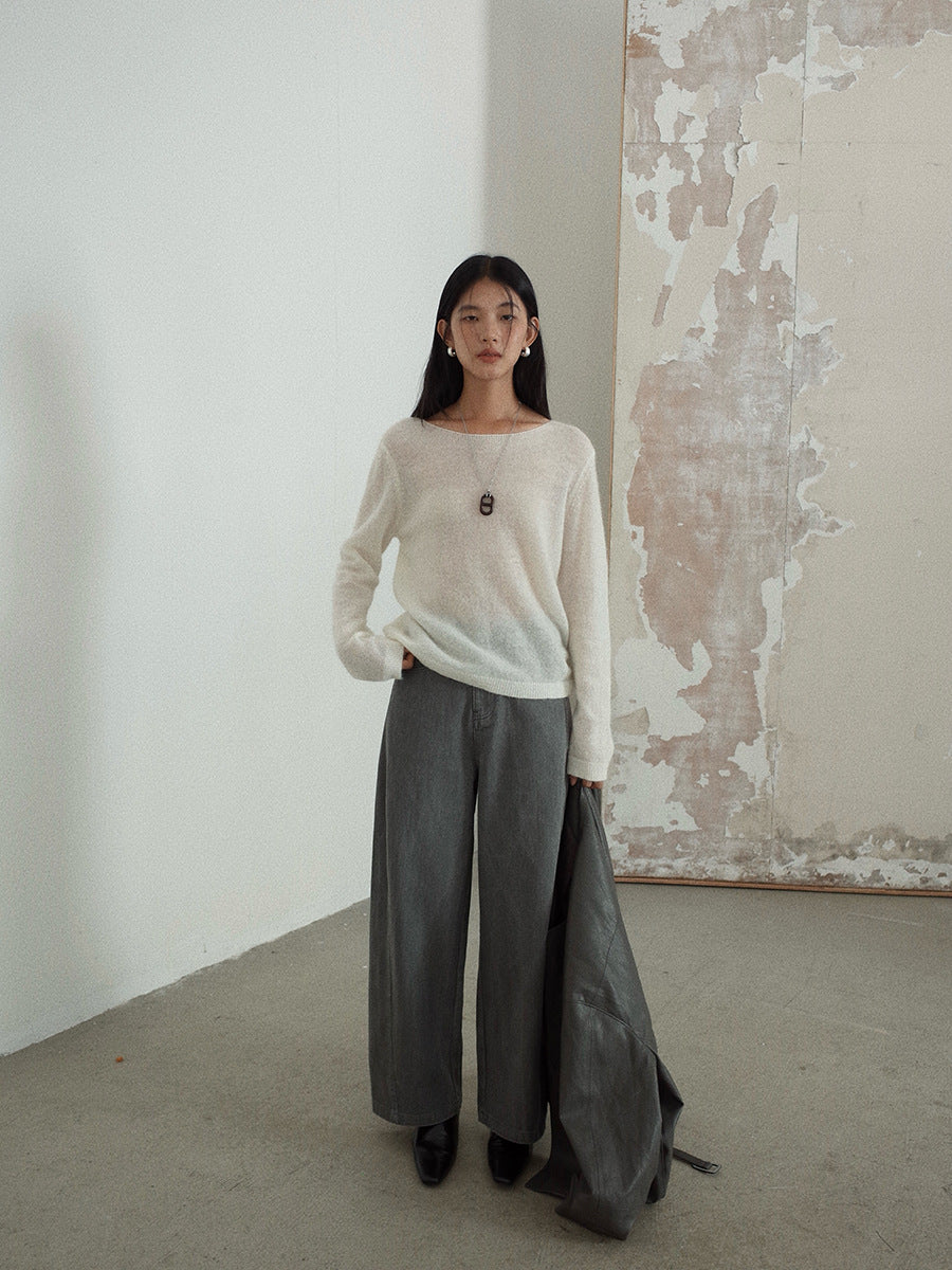 Woman wearing a white wool pullover sweater and gray pants standing in a room with a textured wall.