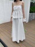 Woman in a white two-piece Raw Edge A-line Maxi Versatile Skirt set outfit standing on a wooden deck with a white wall and greenery in the background.