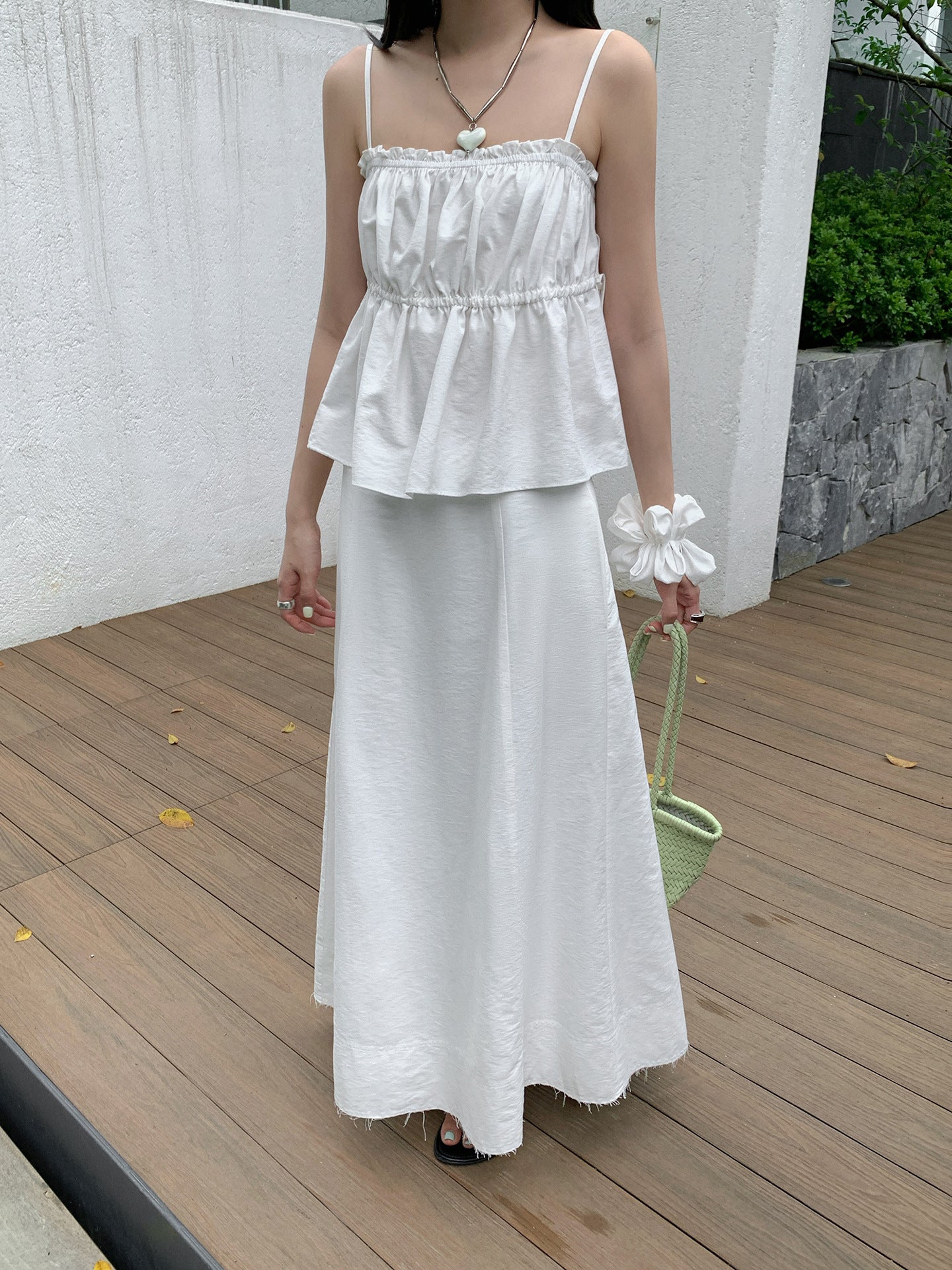 Woman in a white two-piece Raw Edge A-line Maxi Versatile Skirt set outfit standing on a wooden deck with a white wall and greenery in the background.