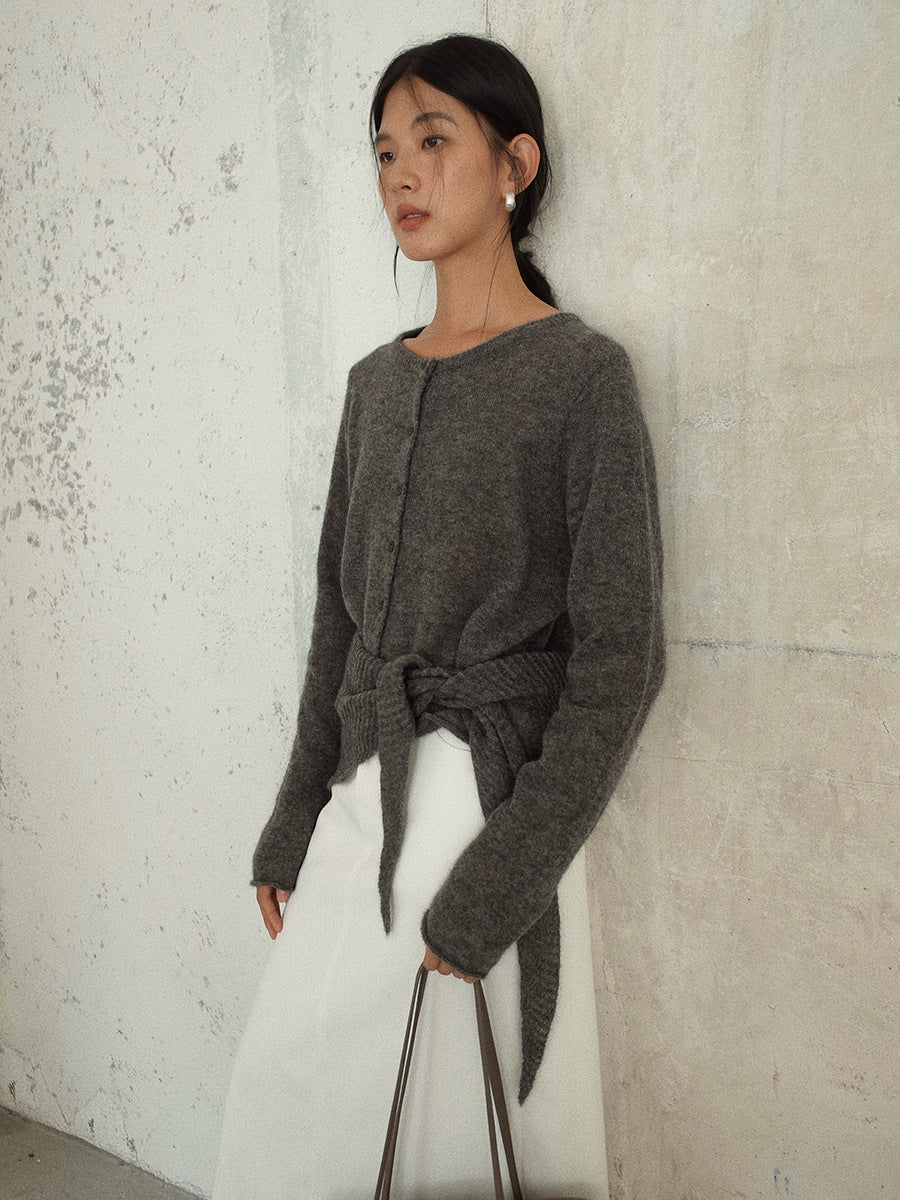 Woman wearing a gray knitted Long Sleeve Knitted Mohair Wool Cardigan Sweater with Scarf against a textured wall.