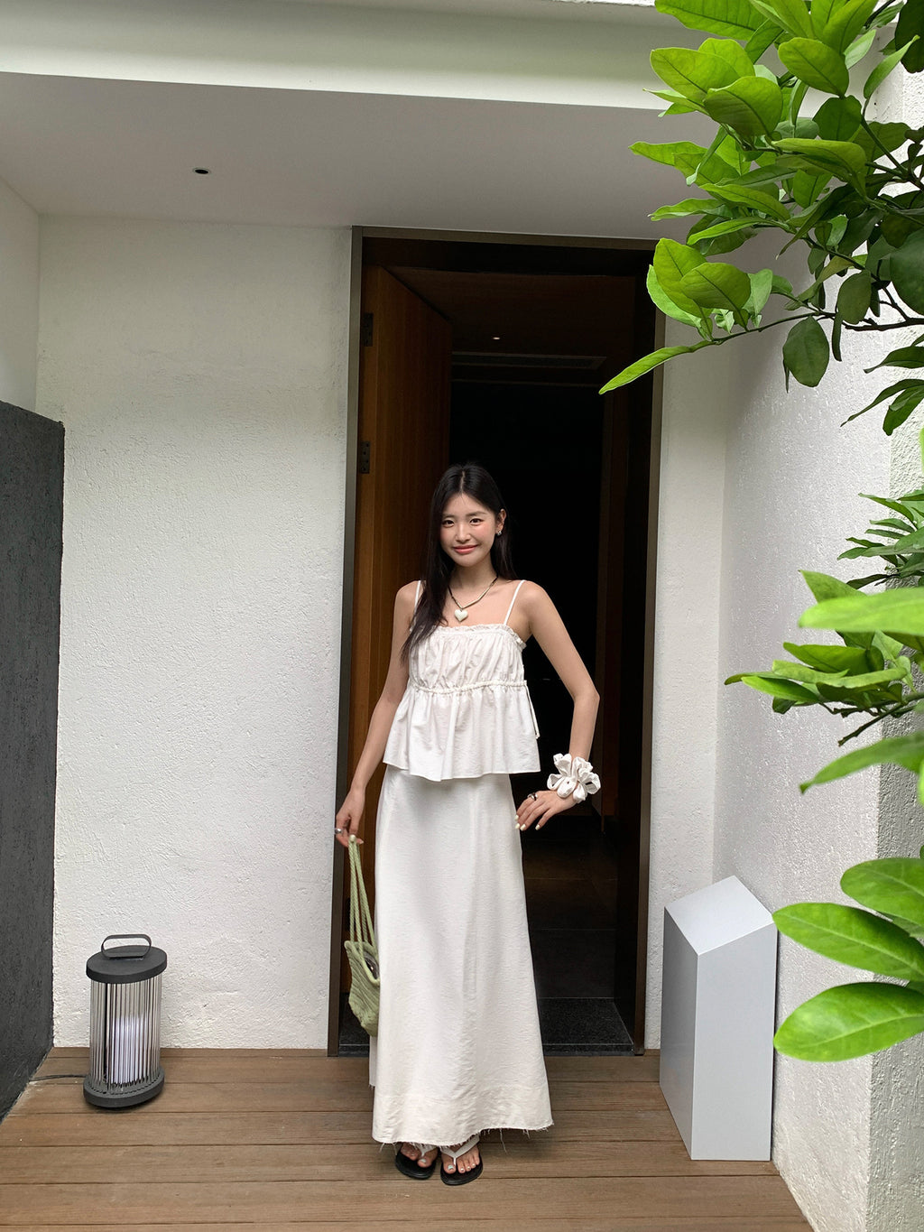 Woman in a white Two-Piece Raw Edge A-line Maxi Versatile Skirt Set standing in a doorway with plants around