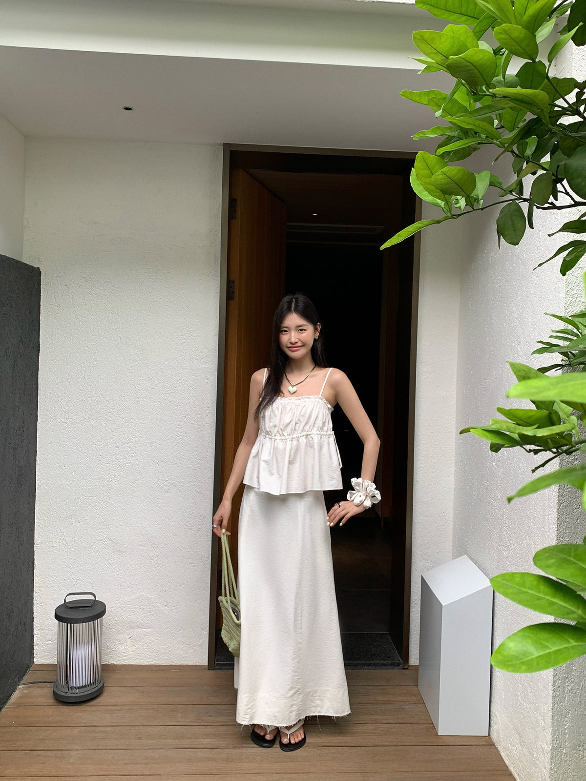 Woman in a white Two-Piece Raw Edge A-line Maxi Versatile Skirt Set standing in a doorway with plants around