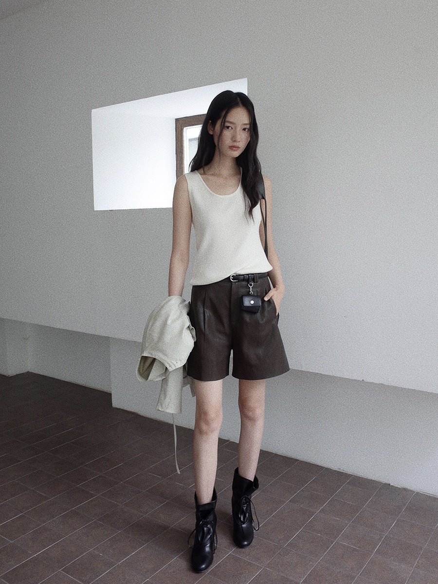 Woman in a white sleeveless top and brown leather shorts standing in a minimalistic room.
