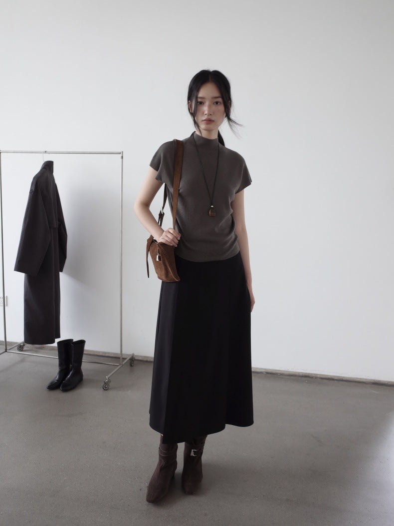 Woman in a brown top and black Maxi Length Drape A-Line Skirt standing in a minimalistic room with a white wall and gray floor.