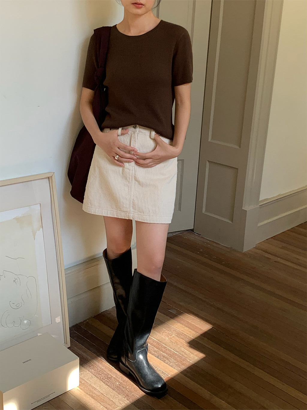 Person wearing a brown top, white Retro Corduroy A-line Short High-waisted mini skirt, and black boots in a room with wooden flooring.