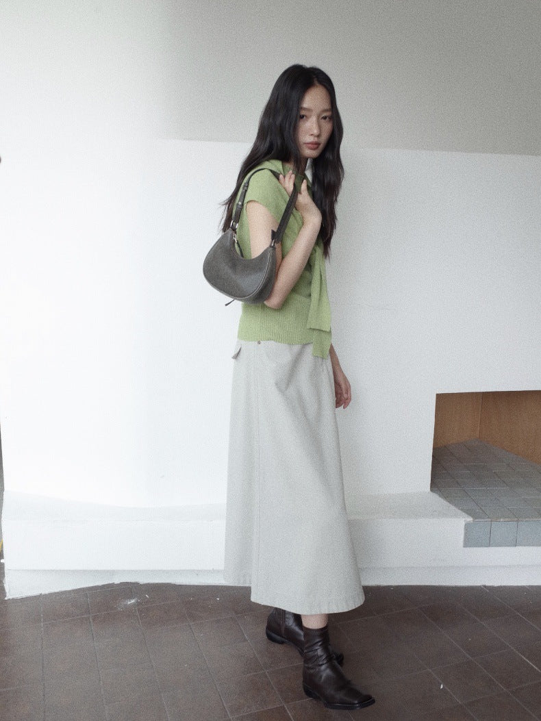 A woman stands indoors wearing a light green short-sleeve top, a long light gray Maxi Length A-Line Denim Skirt, and black ankle boots, while carrying a dark gray shoulder bag.