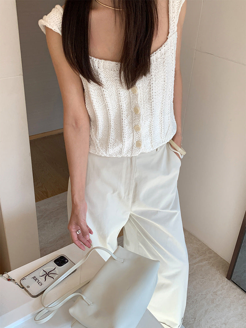 A woman wearing a white Thick Thread Knitted Cardigan Sleeveless Vest Short Tank Top with buttons and matching cream wide-leg pants, holding a white handbag in an indoor setting.