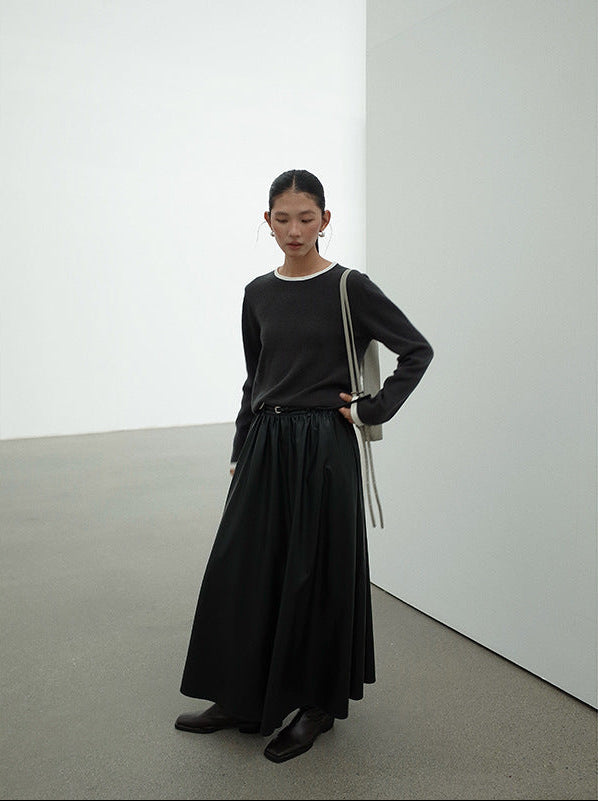 Woman wearing a black Leather Drape Maxi A-Line Skirt standing in a minimalistic room with white walls and gray floor.