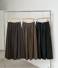 Three Leather Drape Maxi A-Line Skirts in different colors hanging on a rack against a white wall.