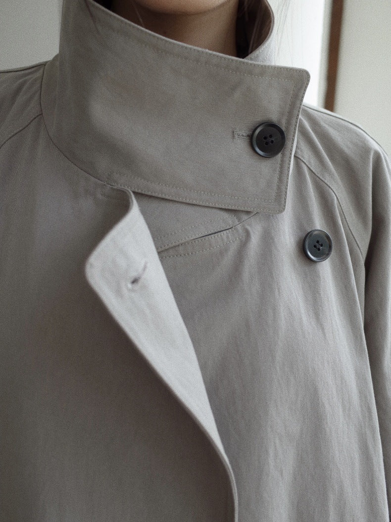Close-up of a person wearing a light gray trench coat with a high collar and dark buttons.