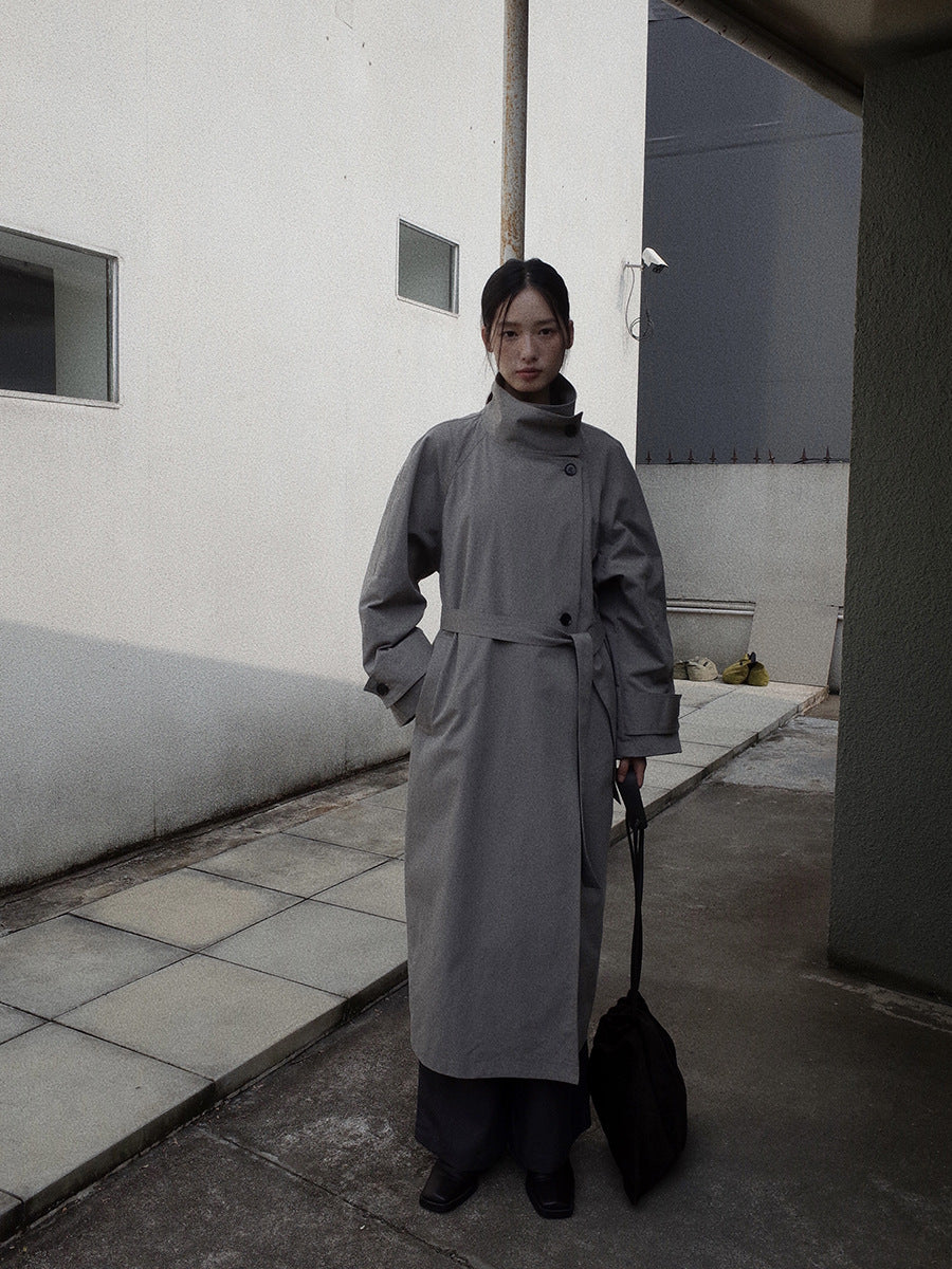 Person wearing a long gray Stand-up Collar Long Trench Coat with Belt holding a black bag on a rooftop.