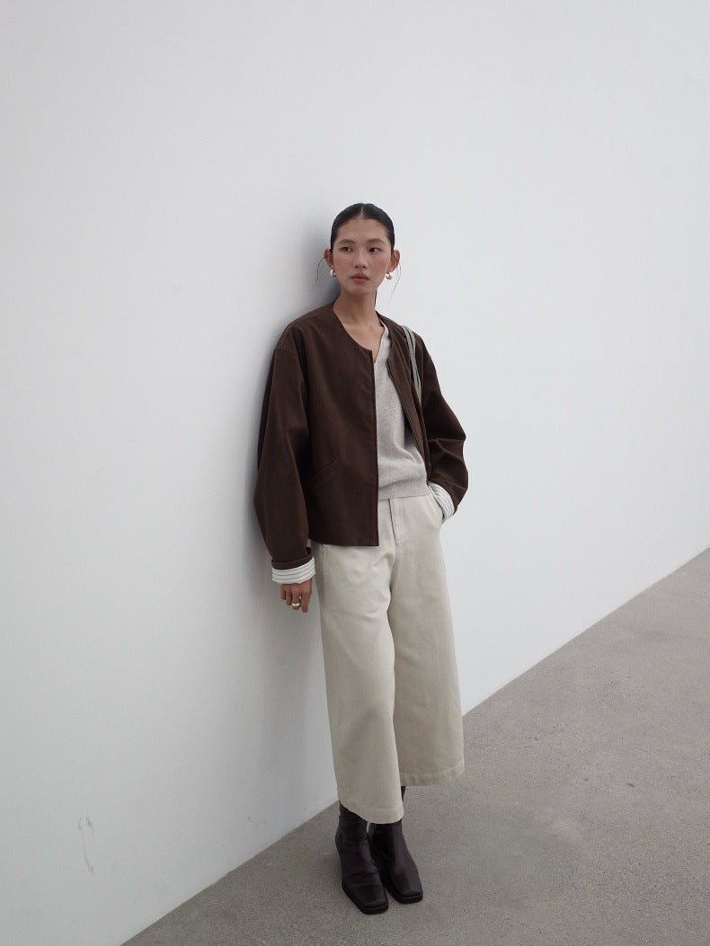 Person wearing a brown jacket and beige wide-leg jeans against a white wall