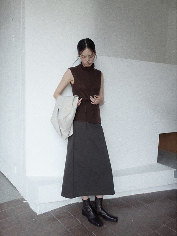 Woman in a brown sleeveless top and black A-line Midi Denim Skirt standing against a white wall.