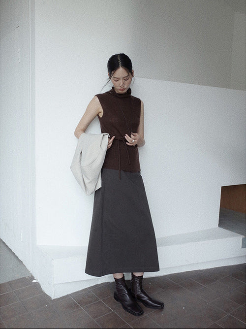 Woman in a brown sleeveless top and black A-line Midi Denim Skirt standing against a white wall.