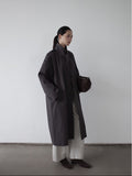 Woman wearing a dark Stand-up Collar Long Relaxed Fit Trench Coat and white pants against a plain background