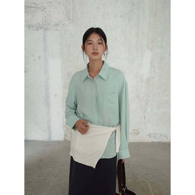 Woman wearing a light green Long-sleeved Relaxed Fit Shirt with a brown bag over one shoulder against a textured wall.