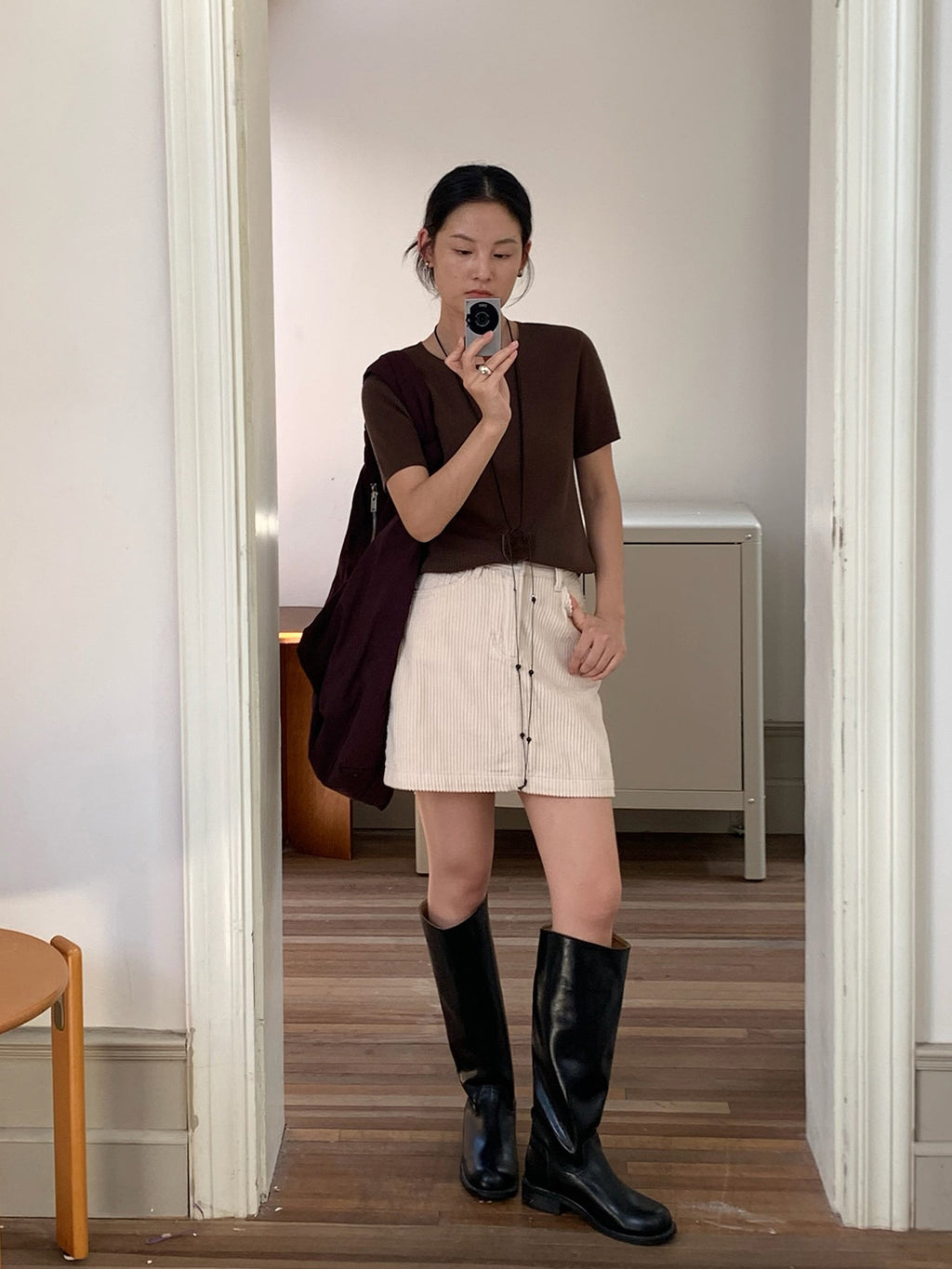 Person taking a mirror selfie wearing a brown top, white Retro Corduroy A-line Short High-waisted mini skirt, and black knee-high boots in a room.