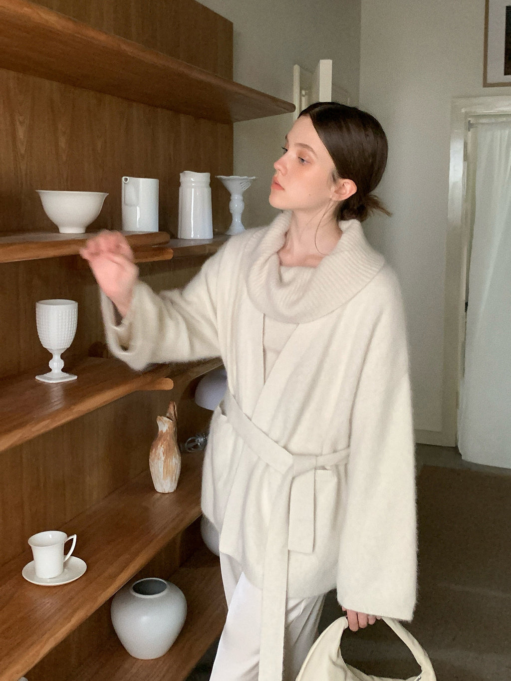 Woman in a Soft Fleece Mid-Thigh Long Cardigan Sweater Robe standing in a room with wooden shelves displaying various ceramic items.