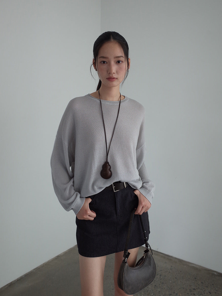 Woman wearing a gray wool sweater and black skirt with a plain background