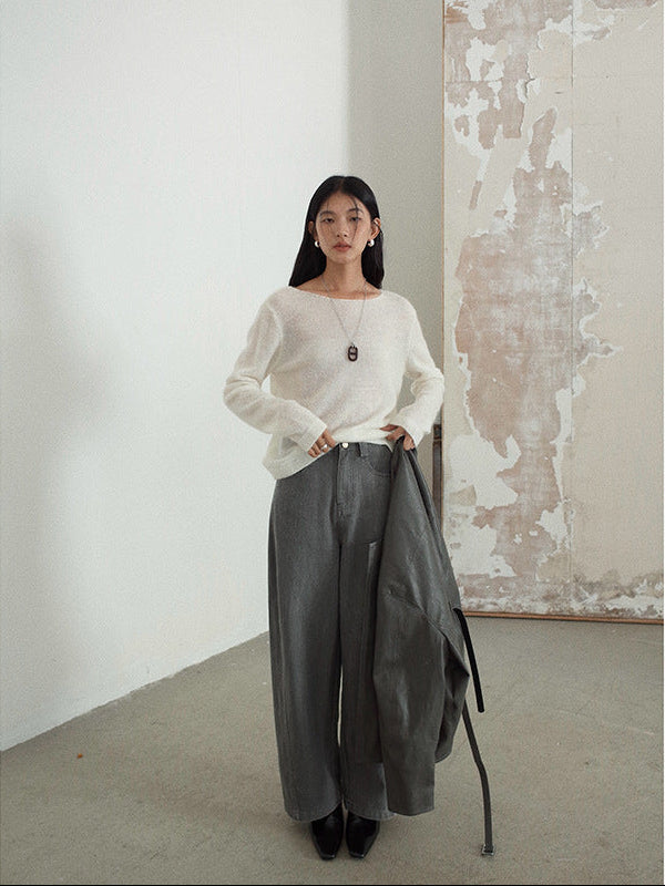 Woman wearing a white wool pullover sweater and gray pants in a minimalistic room.