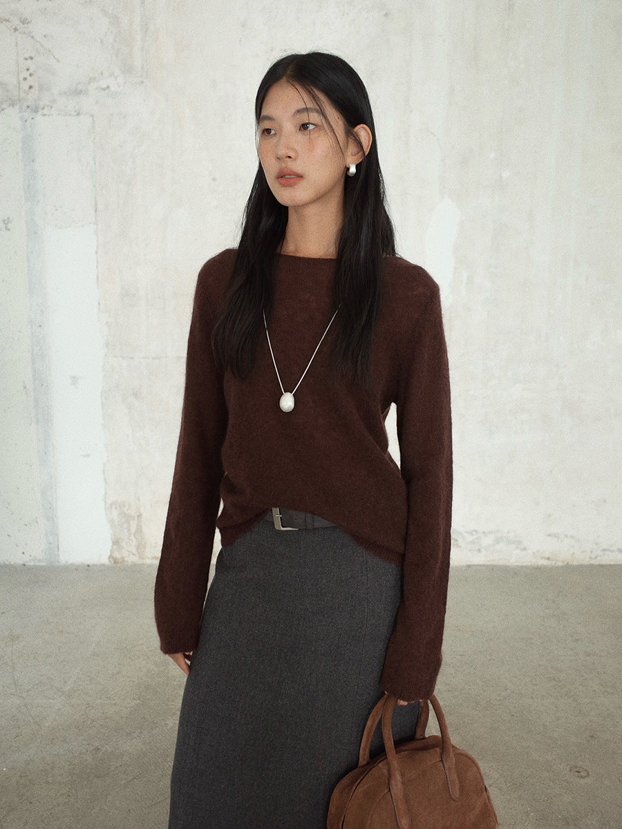 Woman wearing a brown wool pullover sweater and gray skirt with a white background