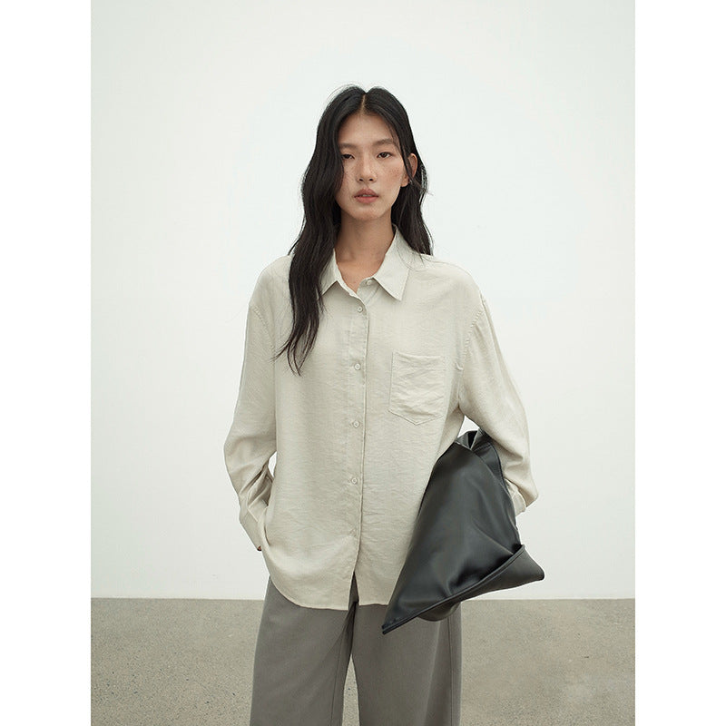 Woman wearing a light-colored Long-sleeved Relaxed Fit Shirt and holding a black bag against a plain background