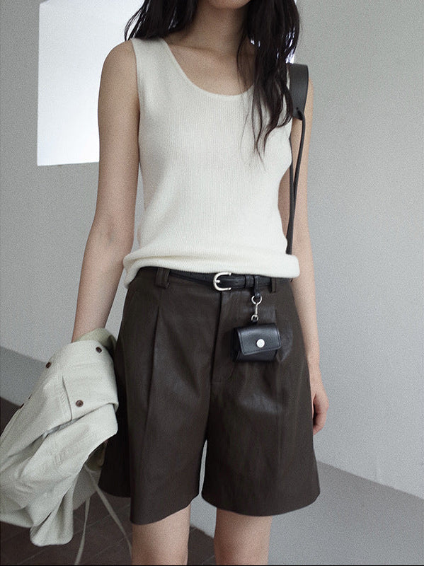 Person wearing a white sleeveless top and brown leather shorts with a small black bag, standing against a plain background.