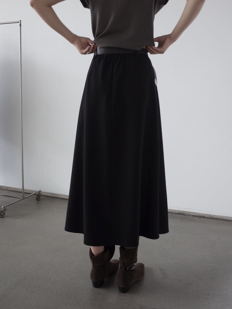A person shown from the back wearing a long black Maxi Length Drape A-Line Skirt, a dark gray top, and brown ankle boots in a minimalist studio setting.