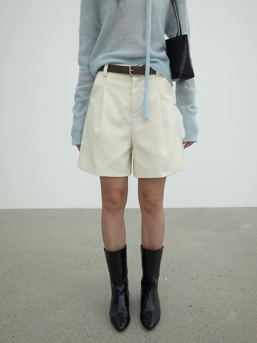 Person wearing a light blue sweater, beige work dress Wide-leg shorts, and black boots against a plain background