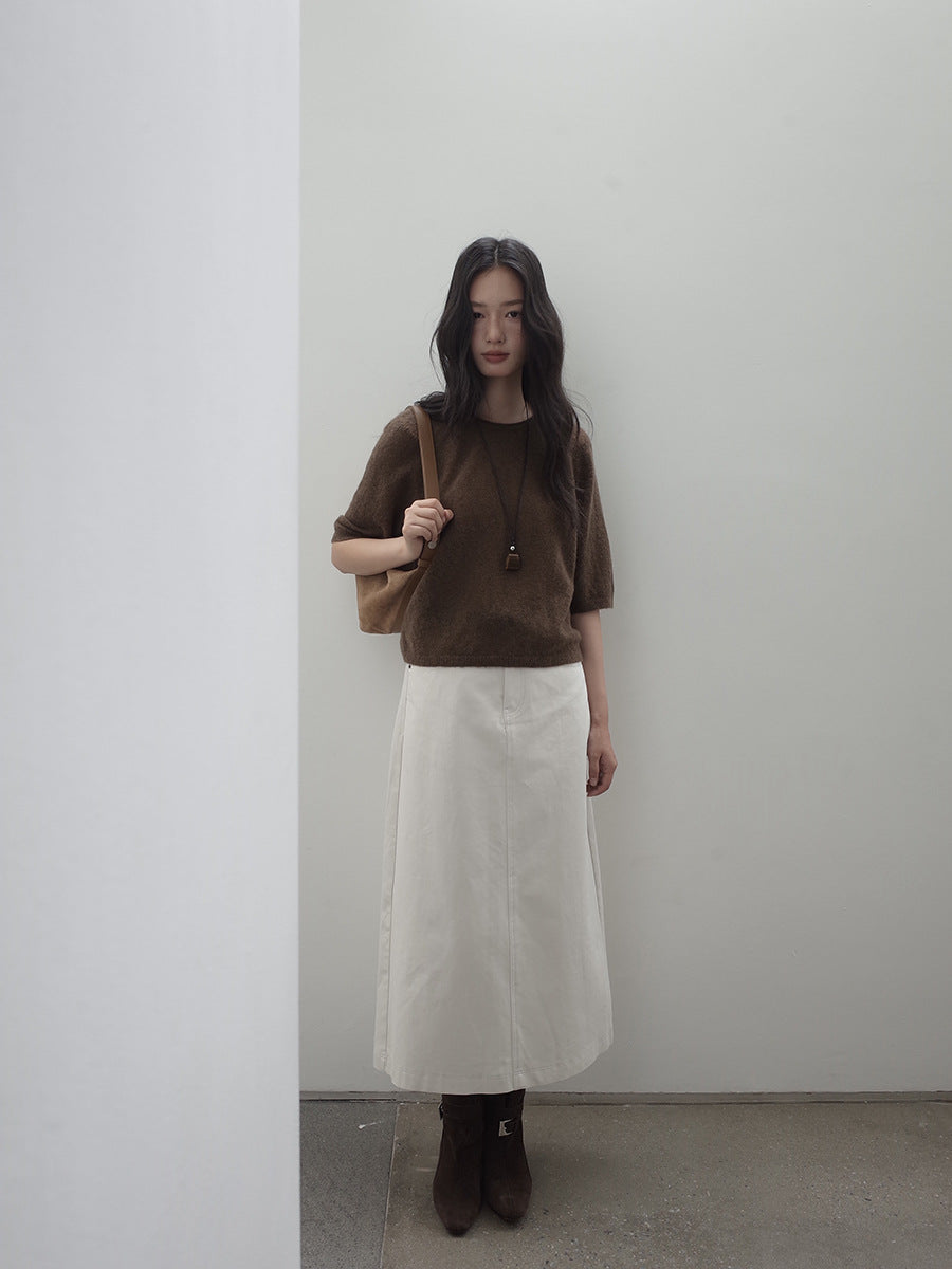 Woman wearing a brown top and white A-line Midi Denim Skirt against a plain wall.