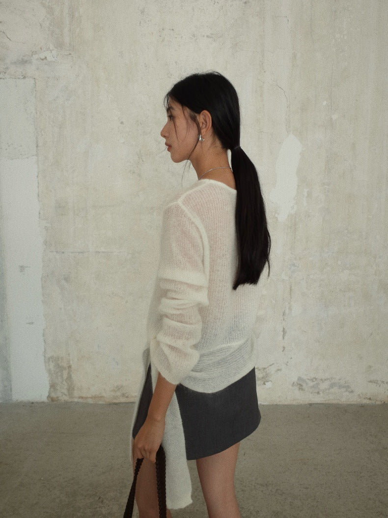 A woman in profile wearing a semi-sheer Strap Waist Long-sleeved Mohair Wool Knitted White Sweater and a dark gray mini skirt, standing against a textured concrete wall.
