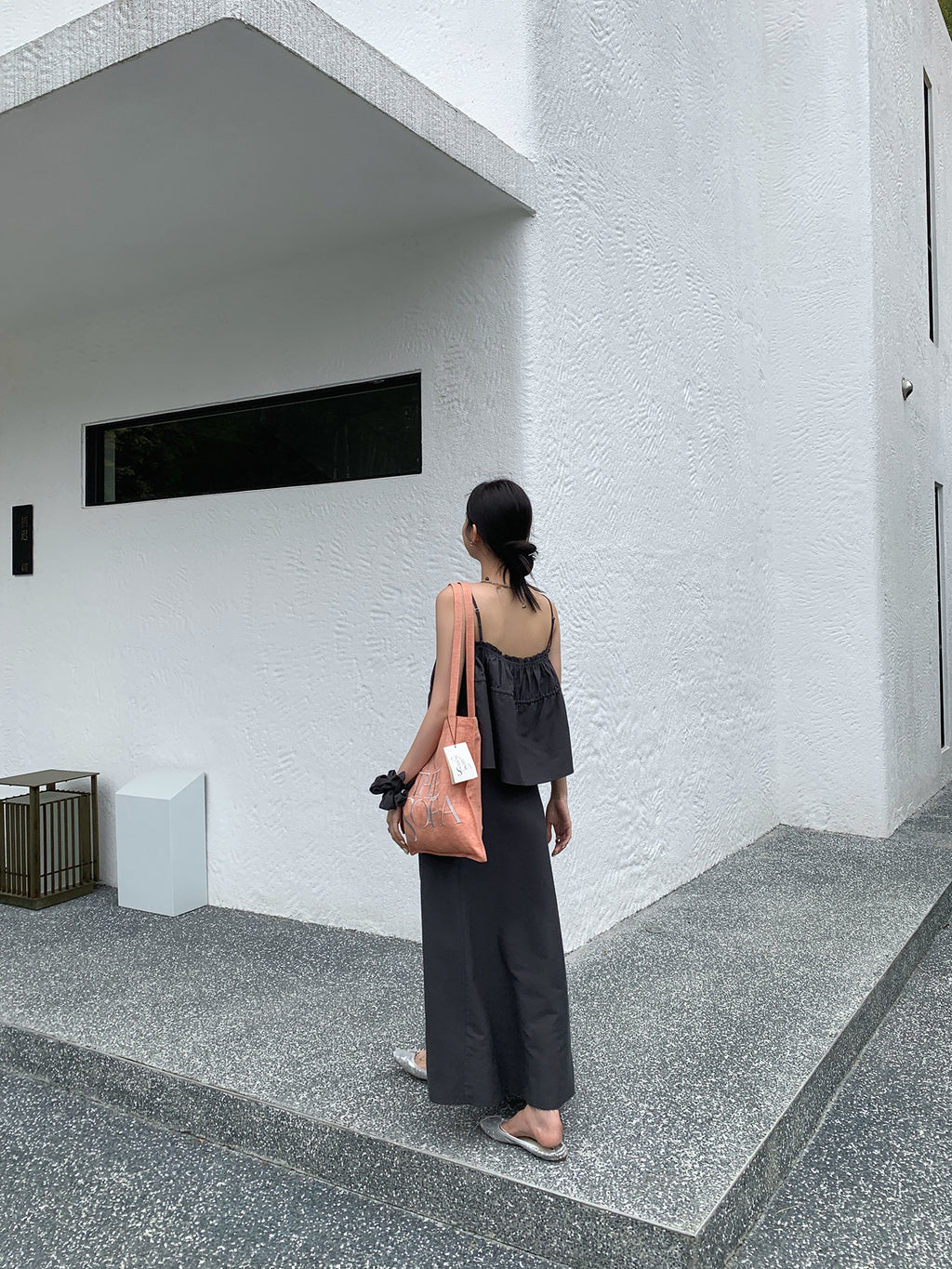 Person standing in front of a modern building with a white wall and geometric design in a black two-piece Raw Edge A-line Maxi Versatile Skirt set.
