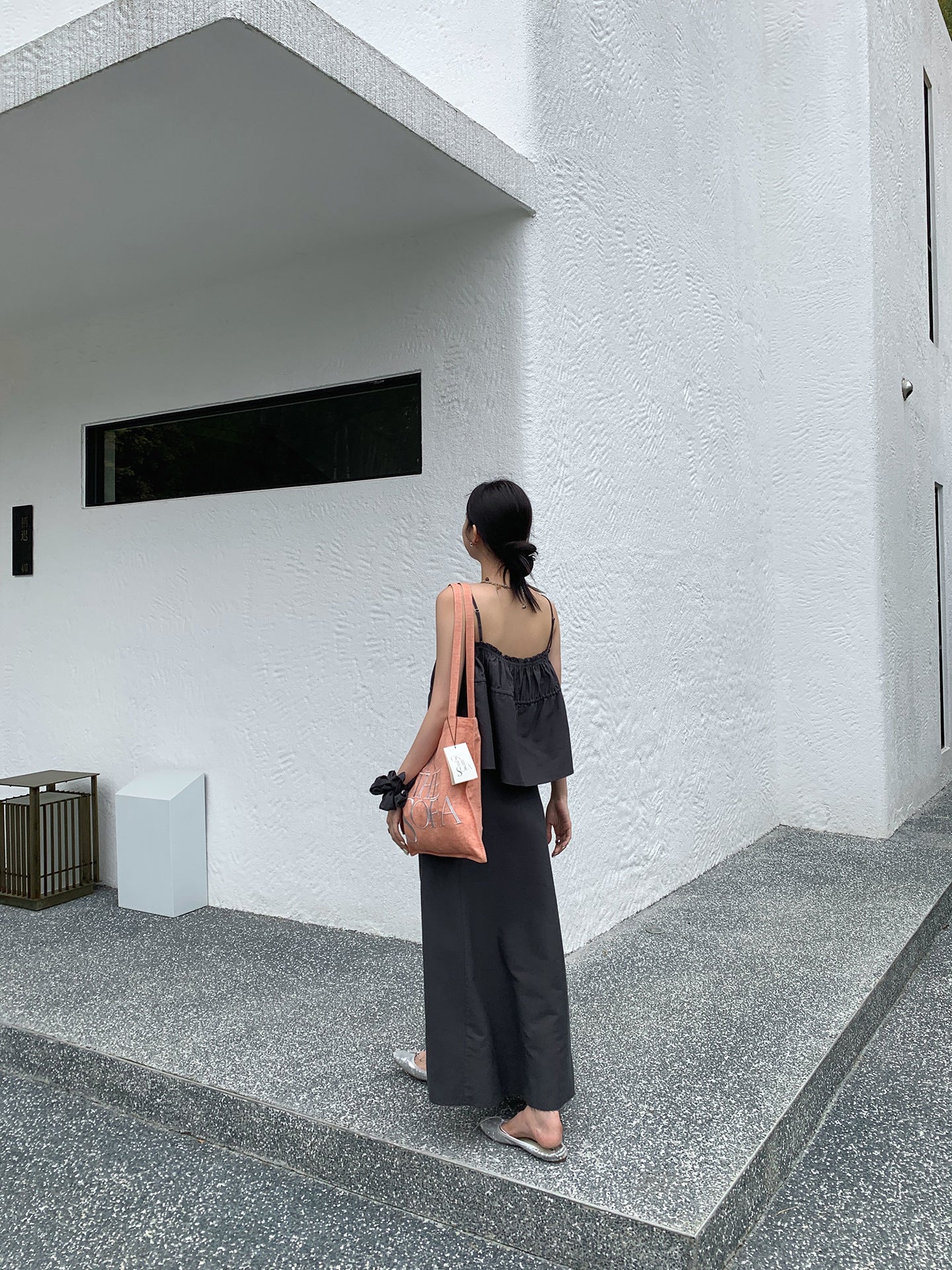 Person standing in front of a modern building with a white wall and geometric design in a black two-piece Raw Edge A-line Maxi Versatile Skirt set.