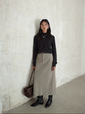 Woman wearing a black top and beige Smooth High-waisted A-line Maxi Skirt against a white wall