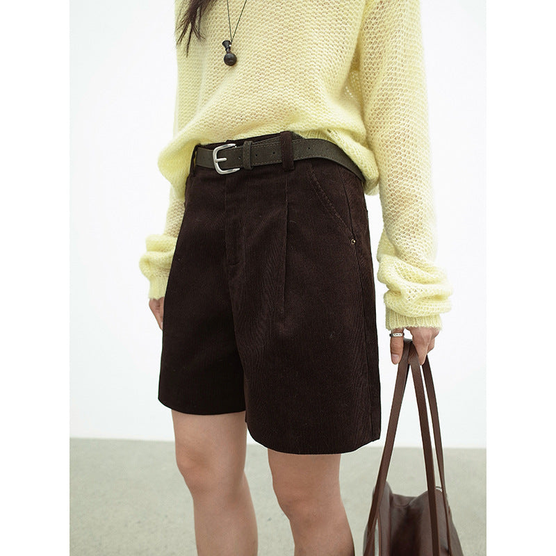 Person wearing a light yellow sweater and dark brown work dress Wide-leg shorts holding a brown bag.