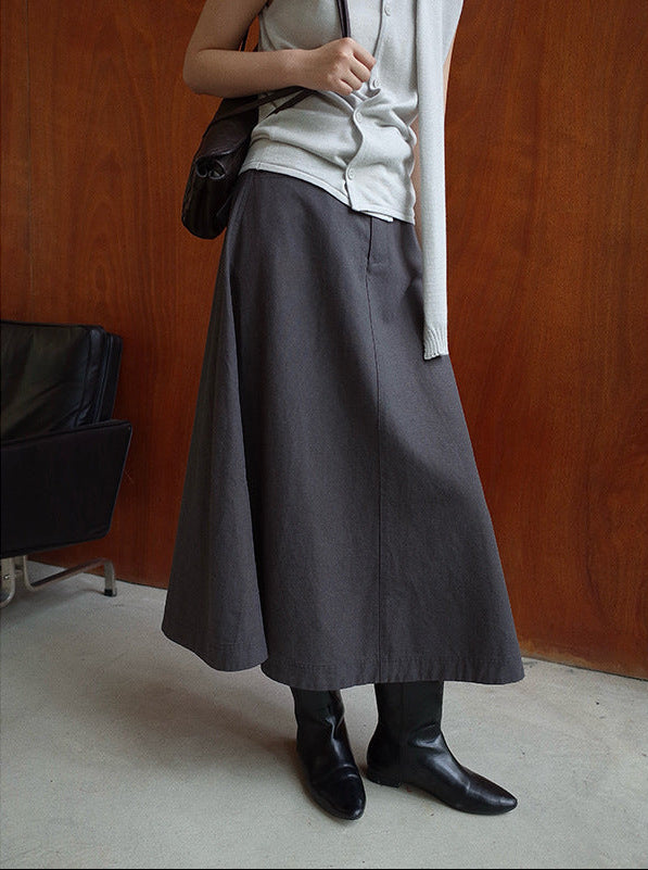 Person wearing a long gray Maxi Length A-Line Denim Skirt and black shoes against a wooden wall.