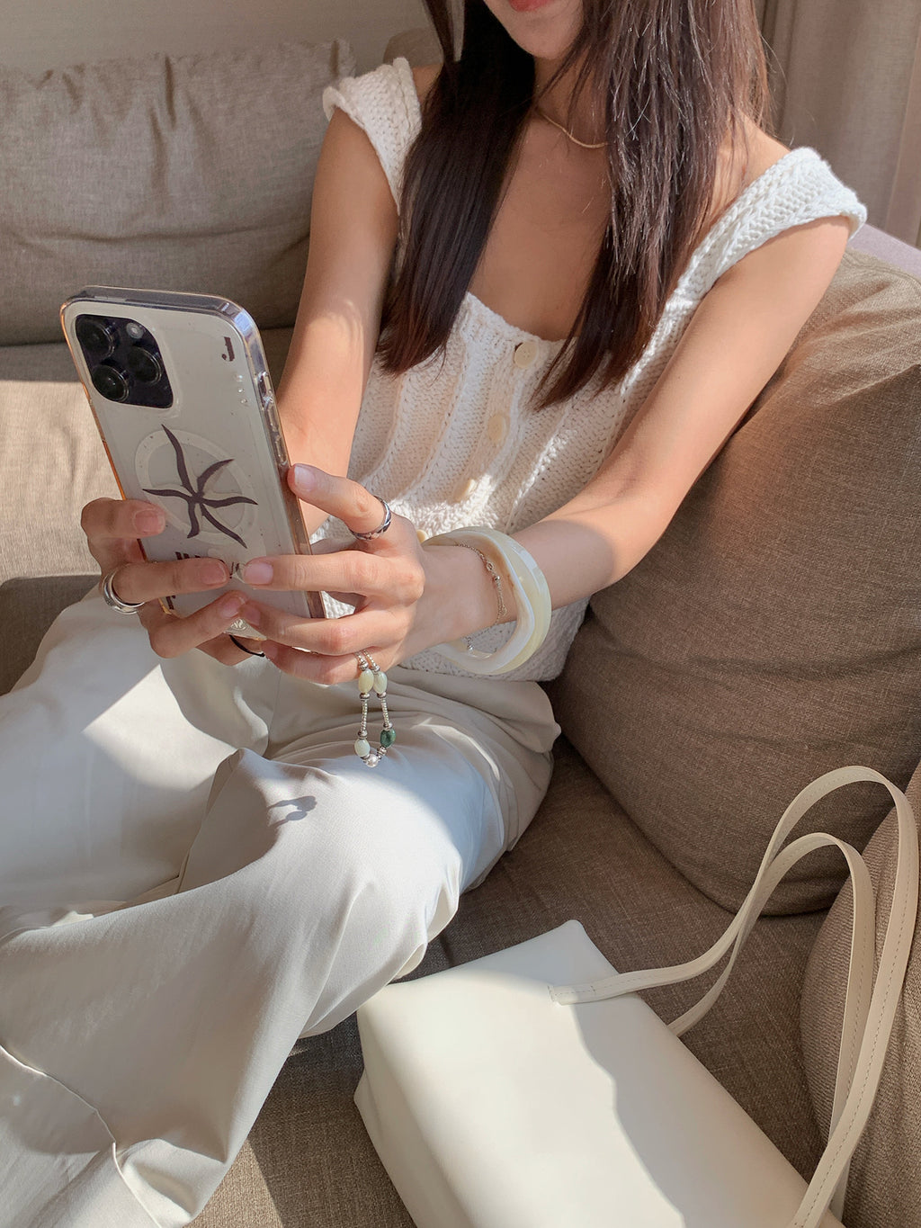 Woman sitting on a couch using a smartphone waering a Thick Thread Knitted Cardigan Sleeveless Vest Short Tank Top with a neutral couch background
