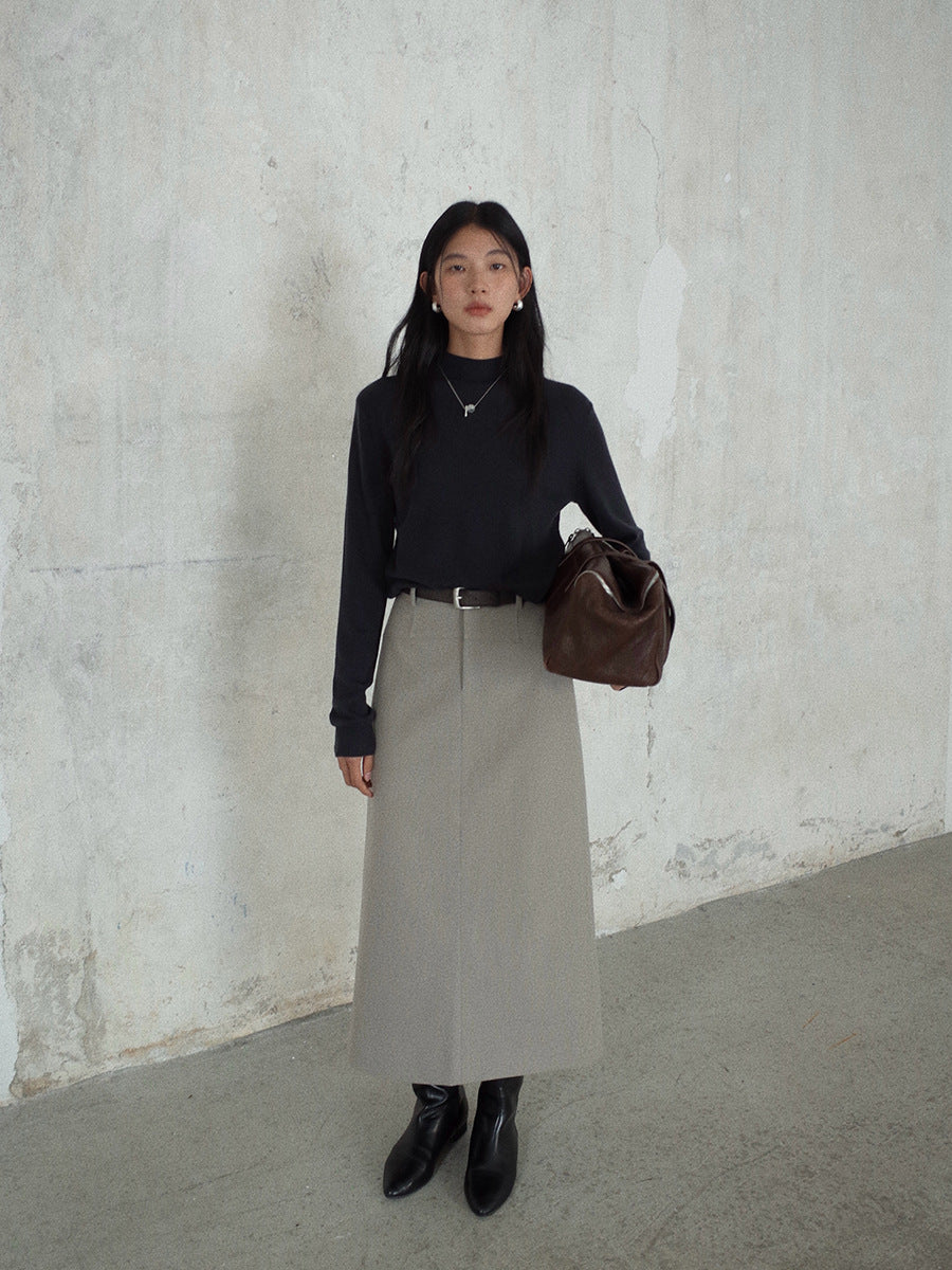 Woman in black top and beige Smooth High-waisted A-line Maxi Skirt holding a brown bag against a plain wall.