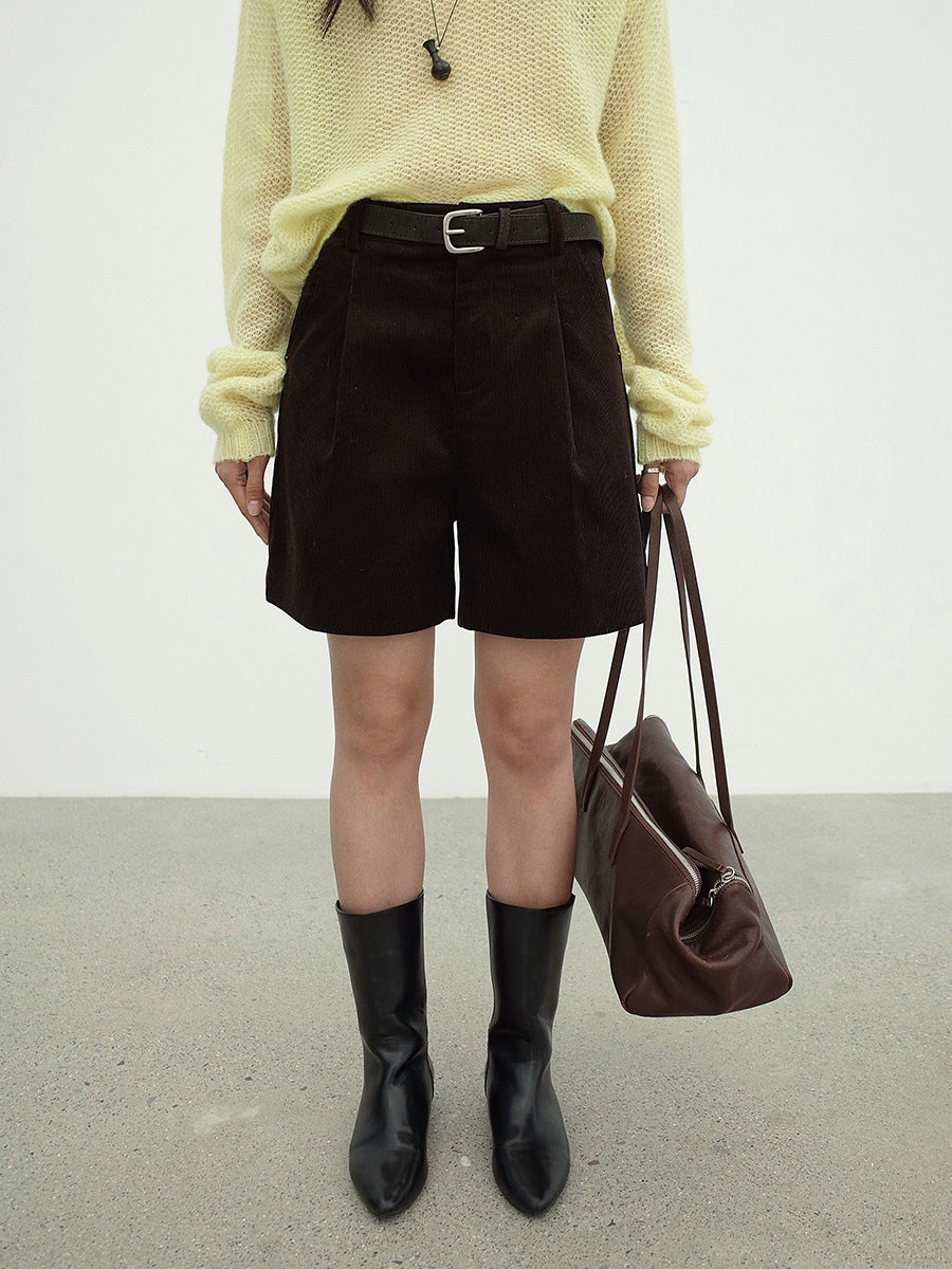 Person wearing a yellow sweater, black work dress Wide-leg shorts, and black boots, holding a brown bag against a plain background.