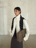Person wearing a white Stand-up Collar Jacket , black and white striped vest, and holding a brown bag against a textured wall.