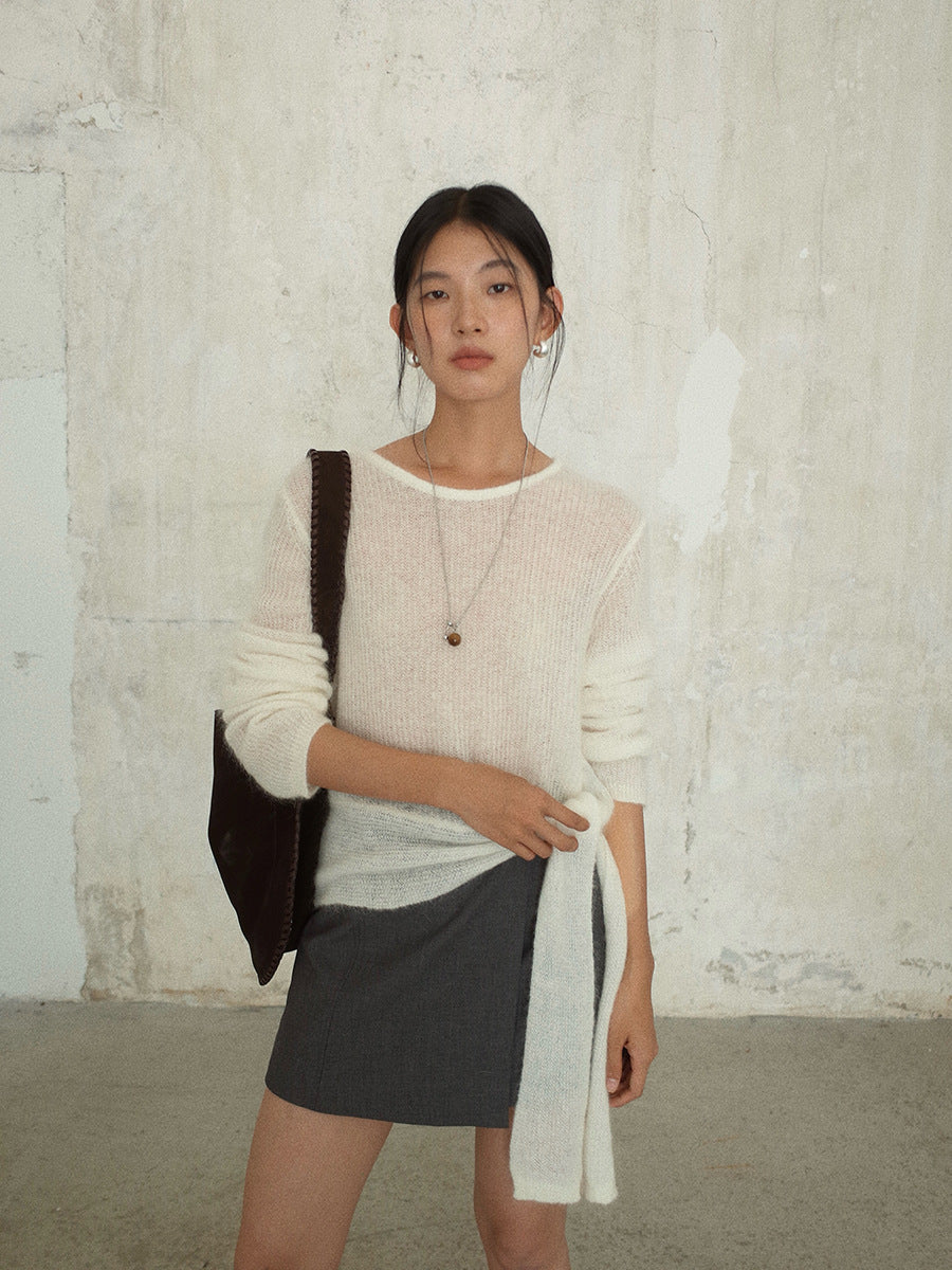 Woman wearing a white Strap Waist Long-sleeved Mohair Wool Knitted Sweater and gray skirt with a black bag against a textured wall.