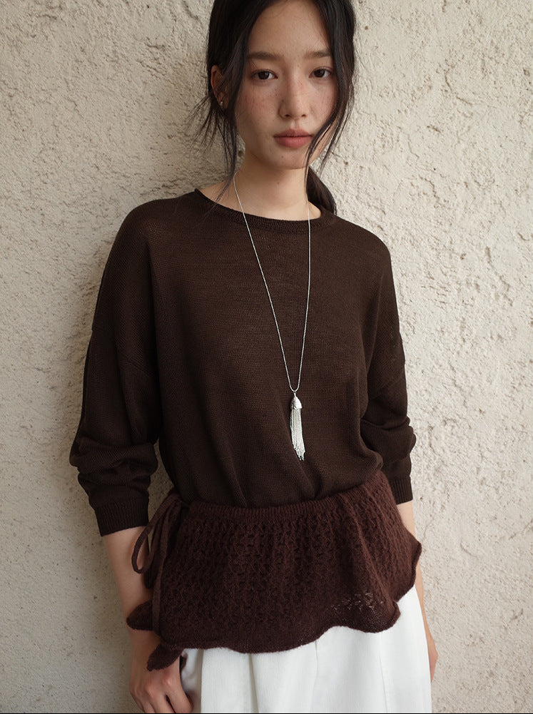 Woman wearing a brown wool sweater with a lace hem against a textured wall.