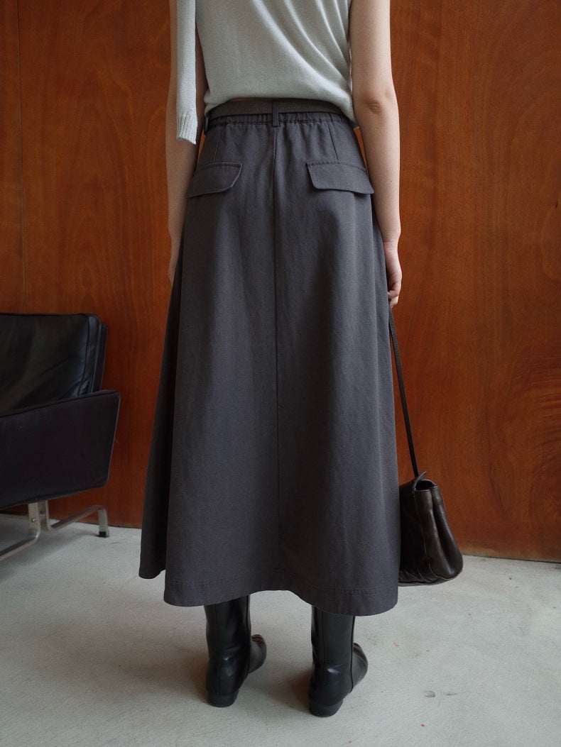 A person shown from the back wearing a dark gray Maxi Length A-Line Denim Skirt with flap pockets, paired with a light gray top and black boots, standing in front of a wooden wall.