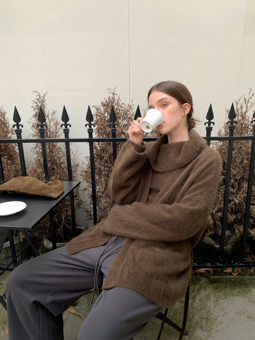 Person sitting outdoors, drinking from a white mug, wearing a brown Soft Fleece Mid-Thigh Long Cardigan Sweater Robe and gray sweatpants.