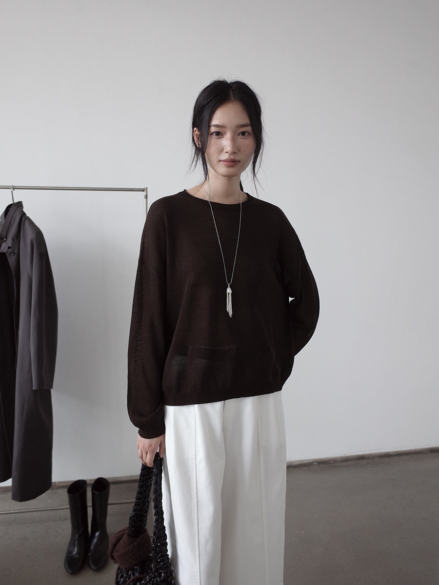 Woman wearing a black wool sweater and white pants standing in a minimalistic room.