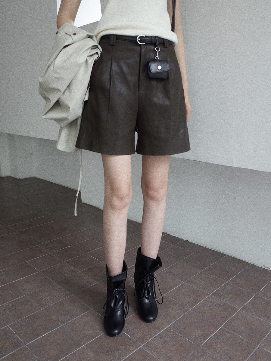 Person wearing brown leather shorts and black boots in a minimal indoor setting